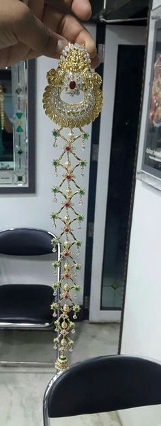 a person holding up a gold and green beaded chandelier in front of a mirror