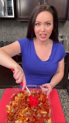 a woman in a blue shirt is cutting into a casserole dish with a red spatula