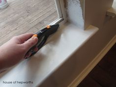 a hand holding a pair of pliers on top of a window sill in front of a door