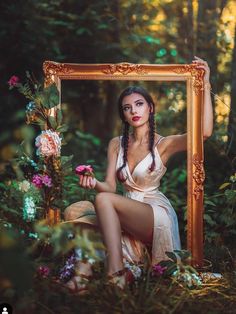 a woman is sitting in the woods holding a frame with flowers on it and posing for a photo