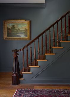 a painting hangs on the wall next to a stair case in a blue painted room