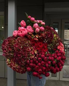 a person holding a bunch of flowers in front of a building with the doors open