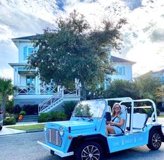 a woman sitting in the back of a blue jeep driving down a street next to a house