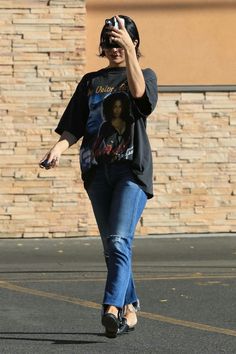 a woman walking across a parking lot holding onto a cell phone to her ear and wearing a helmet