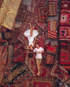 a man and woman laying on rugs in the middle of an area with many different colored carpets