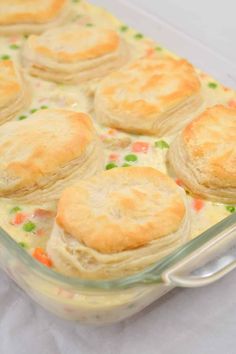 a casserole dish with biscuits and peas in it on a white tablecloth