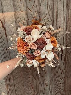 a person holding a bouquet of flowers in front of a wooden wall with planks