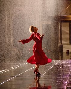 a woman in a red dress is dancing on the floor with water spraying from behind her