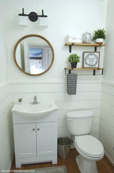 a white toilet sitting next to a sink in a bathroom under a mirror and shelves