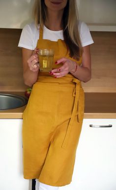 a woman in an apron holding a glass with something in it and looking at the camera