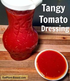 a small bowl of sauce next to a large red vase on a cutting board with a white lid