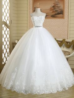 a white ball gown on display in a room with wooden flooring and wallpaper