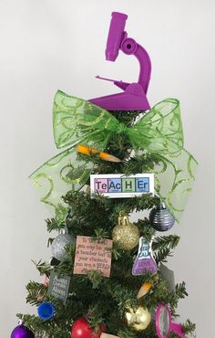 a small christmas tree decorated with ornaments and writing on the top, in front of a white wall