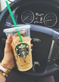 a person holding a starbucks drink in their hand while sitting in the driver's seat of a car