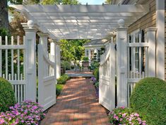 a white pergolated walkway leading to a house with flowers and shrubs on either side