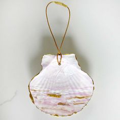 a pink and gold shell ornament hanging on a white wall next to a string