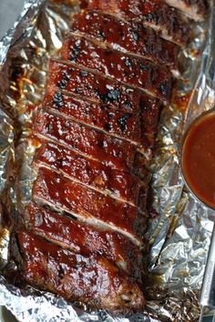 ribs covered in bbq sauce on tin foil next to a bowl of ketchup