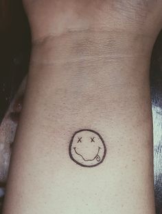 a small smiley face tattoo on the left side of the arm, with stars around it