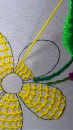 a close up of a piece of embroidery on a white cloth with yellow and green thread