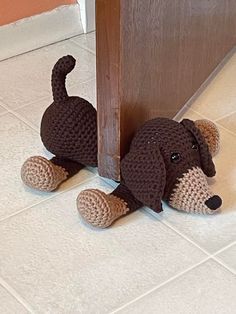 a crocheted dog sitting on the floor in front of a door with its tail up