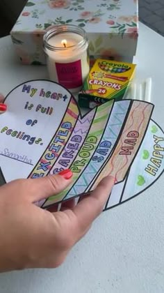 a person holding a heart shaped paper with words on it and a candle in the background