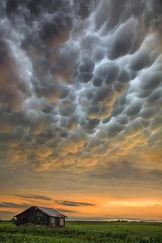 the sky is filled with clouds over an old barn and farm in the distance at sunset