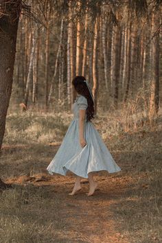 a woman in a blue dress is walking through the woods with her back to the camera