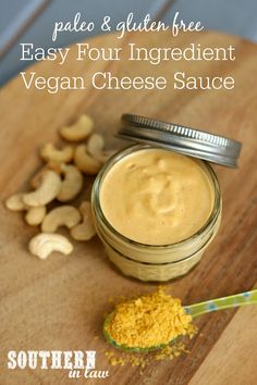 a jar filled with vegan cheese sauce on top of a wooden cutting board next to cashews