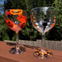 two wine glasses decorated with pumpkins and black dots, sitting on a wooden table