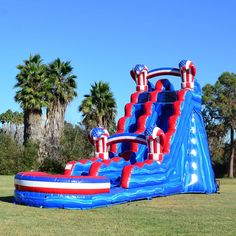 an inflatable water slide with red and white stripes on it is sitting in the grass near palm trees