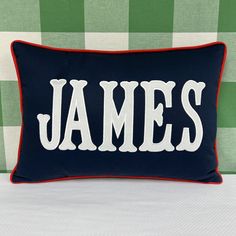 a pillow with the word james on it in white and red stitching sitting on a green checkered wall