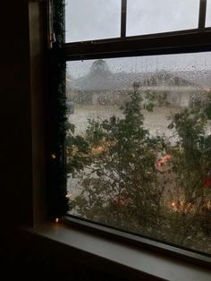 a window with rain falling down on the ground and trees in front of it as seen from inside