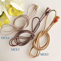 three different types of beaded hair ties on a table with flowers in the background