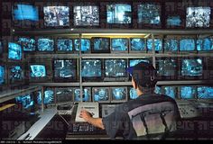 a man sitting at a desk in front of many televisions with blue images on them