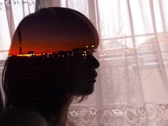 a woman standing in front of a window with the sun setting behind her and looking out