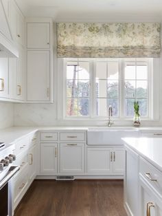 a kitchen with white cabinets and counter tops, wood flooring and a window above the sink