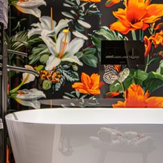 a white bath tub sitting next to a wall with orange flowers on it's side