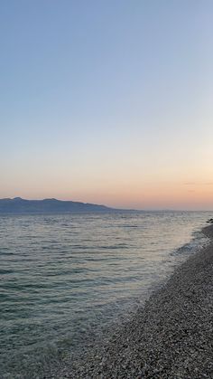 there is a bench on the beach by the water's edge at sunset or dawn