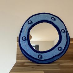 a blue circular mirror sitting on top of a wooden shelf next to a white wall