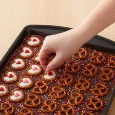 a person placing pretzels on top of a tray with hearts and sprinkles