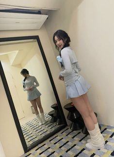 a woman standing in front of a mirror with her legs crossed and looking at herself