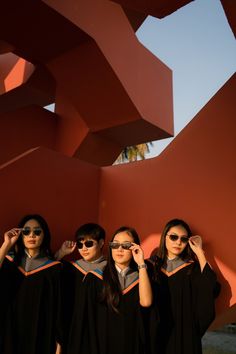 three girls in graduation gowns and sunglasses are posing for the camera with their hands on their ears