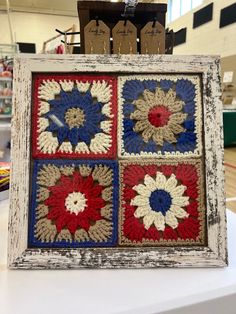 an old frame has four squares with red, white and blue crocheted flowers