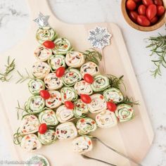 a christmas tree shaped appetizer on a cutting board next to tomatoes and herbs