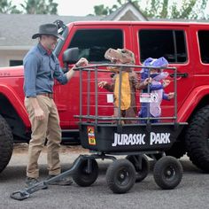 a man standing next to a red truck with kids in it's cage on the back