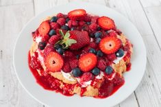 a white plate topped with cake covered in berries and whipped cream on top of it