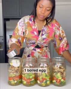 a woman standing in front of four jars filled with different types of vegetables and nuts