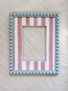 a pink and white striped photo frame on a beige background with blue beads around the edges