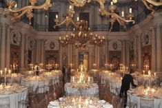 a large room with many tables and chairs covered in white tablecloths, gold chandeliers and candles