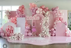 a pink and white stage set up for a birthday party with balloons on the walls